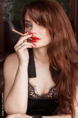 A beautiful sexy woman in a black dress smokes a cigarette and drinks whiskey. Mistress  Spy Girl