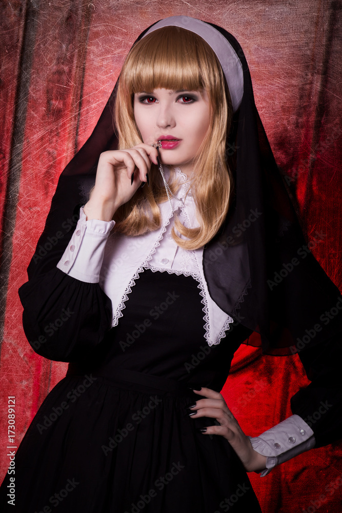 Religious nun in the concept of religion on a red background. Blonde with red eyes and dark makeup, vampire, demon. Costume for Halloween Religious nun in the concept of religion on a red background. Blonde with red eyes and dark makeup, vampire, demon. Costume for Halloween