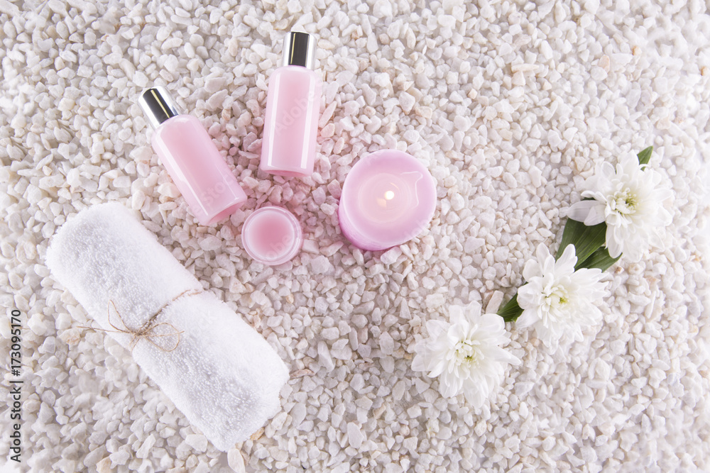 Spa. Still life. Candle, bottles with cream of pink color, a towel and flowers on a background of white pebbles. Top view Spa. Still life. Candle, bottles with cream of pink color, a towel and flowers on a background of white pebbles. Top view