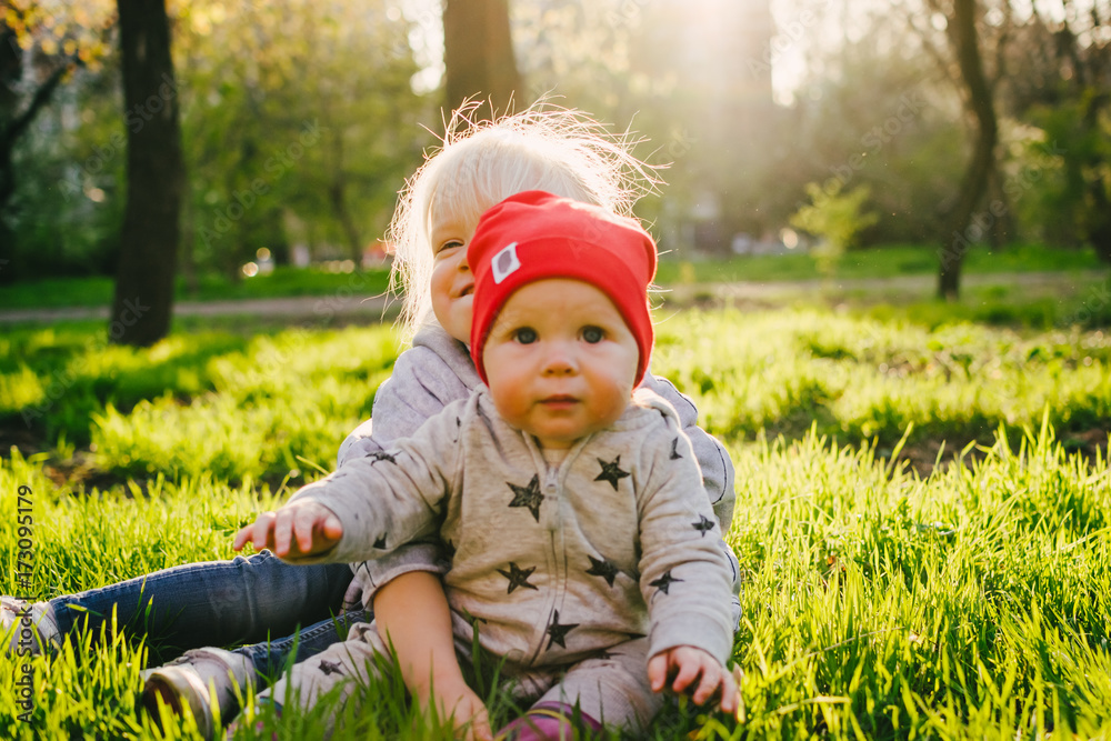 Two cute little sisters having fun together on the grass on a sunny spring day