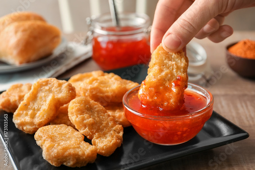 Person dipping chicken nugget in chili sauce indoors