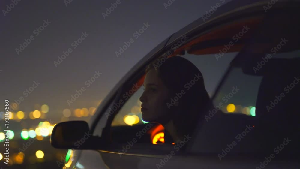 The woman sit in a car on the background of the city. evening night time