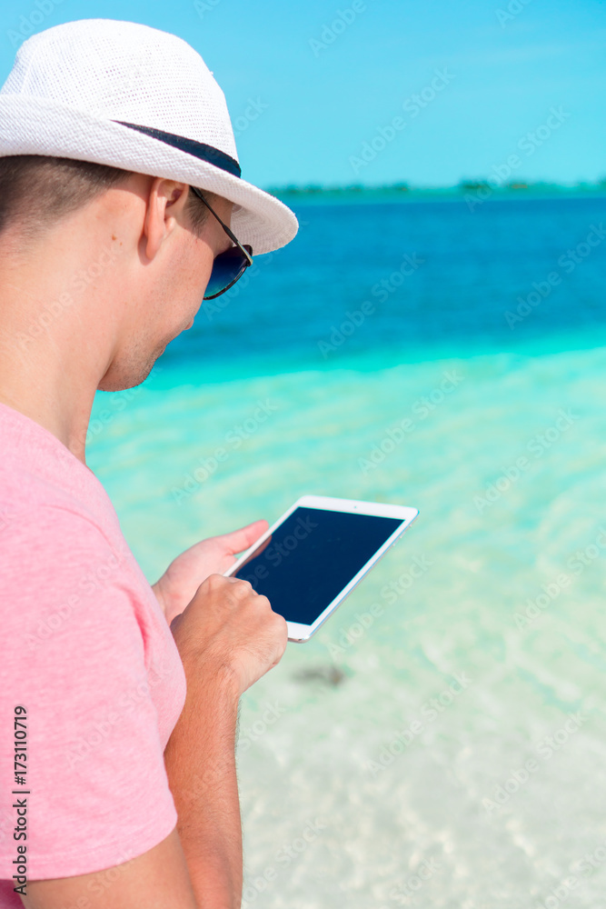 Young man with laptop on the background of turquoise ocean at tropical beach take a photo of starfish in natural reserve