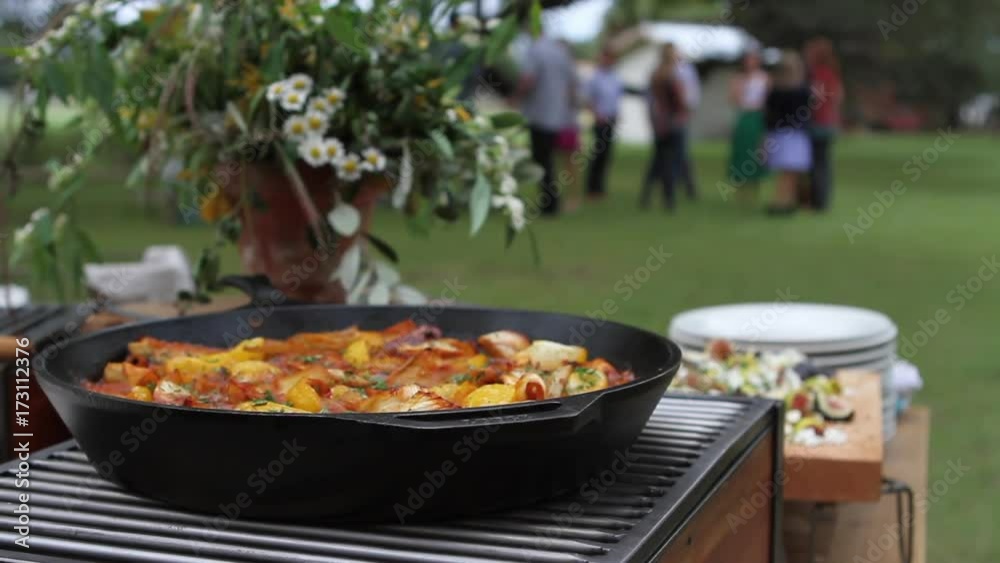 Person places casserole in skillet on picnic table, close up Person places casserole in skillet on picnic table, close up