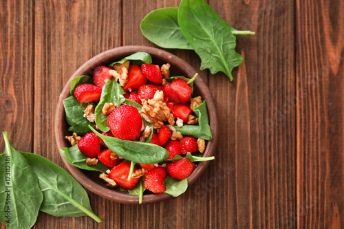 Plate of salad with spinach, strawberry and walnuts on table