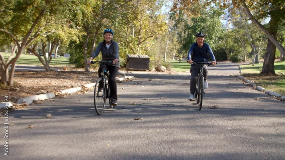Senior Couple Cycling Through Park In Slow Motion
