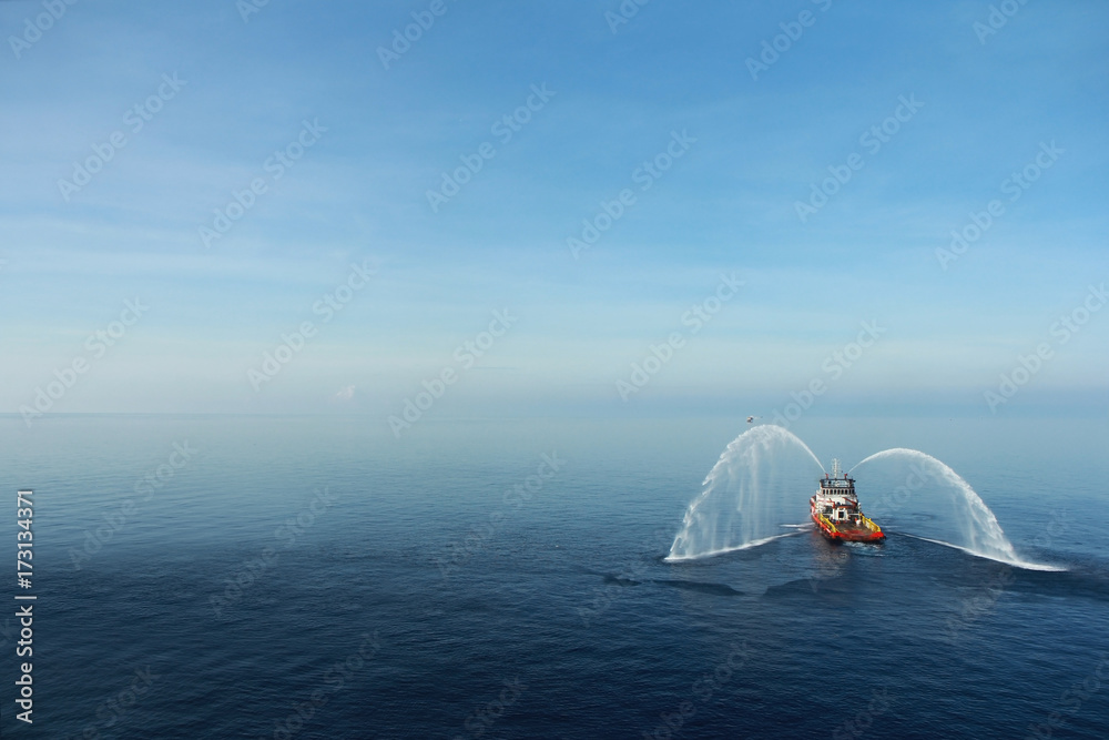 Obraz premium Fire hose boat is spraying water on the sea for supporting emergency case of fire of offshore oil and gas industry. Fire fighting boat sprays water on the sea.