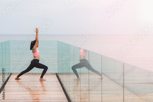Asian women play yoga on a wooden deck by the sea in the morning. With reflection in the mirror.