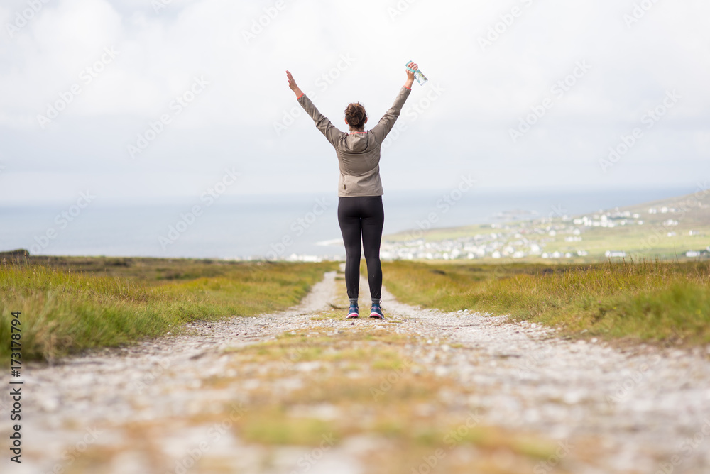 Young woman on a walkway back facing rising arms Young woman on a walkway back facing rising arms