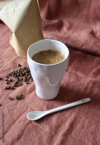 Coffee cup in white pottery mug, scattered coffee beans from paper package