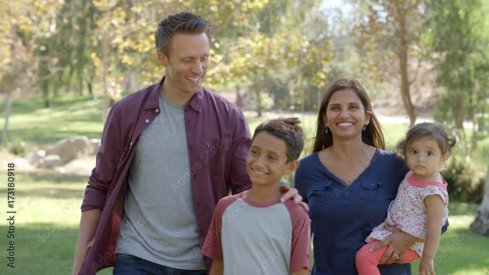 Happy mixed race family walking into focus together in park Happy mixed race family walking into focus together in park