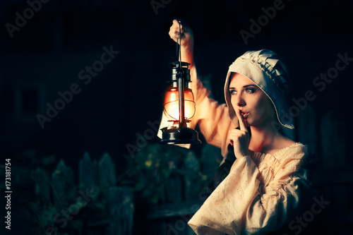 Fototapeta Medieval Woman with the Finger on the Lips Holding a Lamp