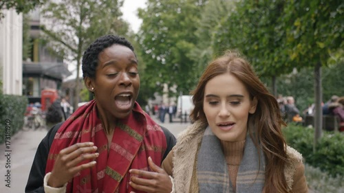 Camera leads in front of two diverse female friends walking and talking in the city
