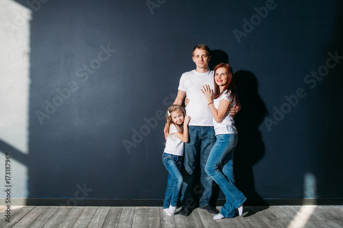 Happy family portrait standing on gray background wooden floor room window sunny day