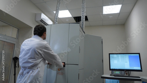 Man in lab coat opening the lid of the machine in the factory. Scientist opens the equipment © Media Whale Stock
