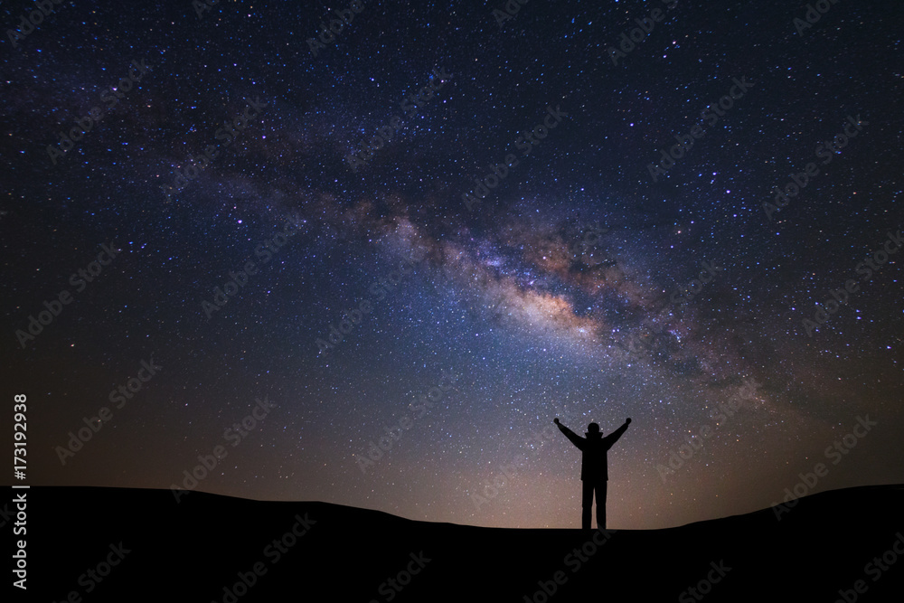 Naklejka premium Landscape with milky way galaxy and space dust in the universe, Night sky with stars and silhouette of a standing sporty man with raised up arms on high mountain.