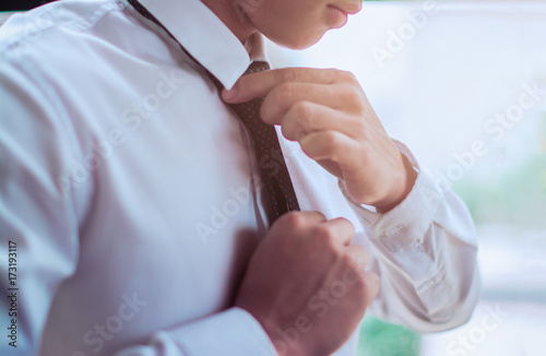 The businessman ties a black tie  in white shirt.