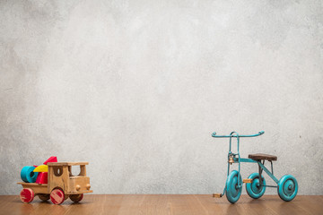 Retro old toy tricycle and obsolete wooden truck with construction blocks front concrete textured wall background. Vintage style filtered photo