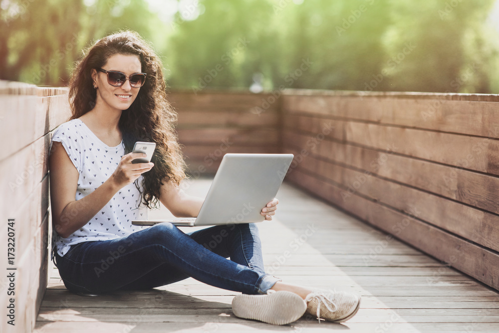 Beautiful student girl working on laptop outdoor. Young woman using smartphone and laptopcomputer in the park Beautiful student girl working on laptop outdoor. Young woman using smartphone and laptopcomputer in the park
