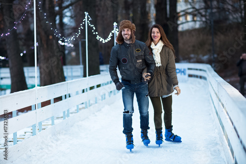 Young happy loving couple skating at ice rink outdoors