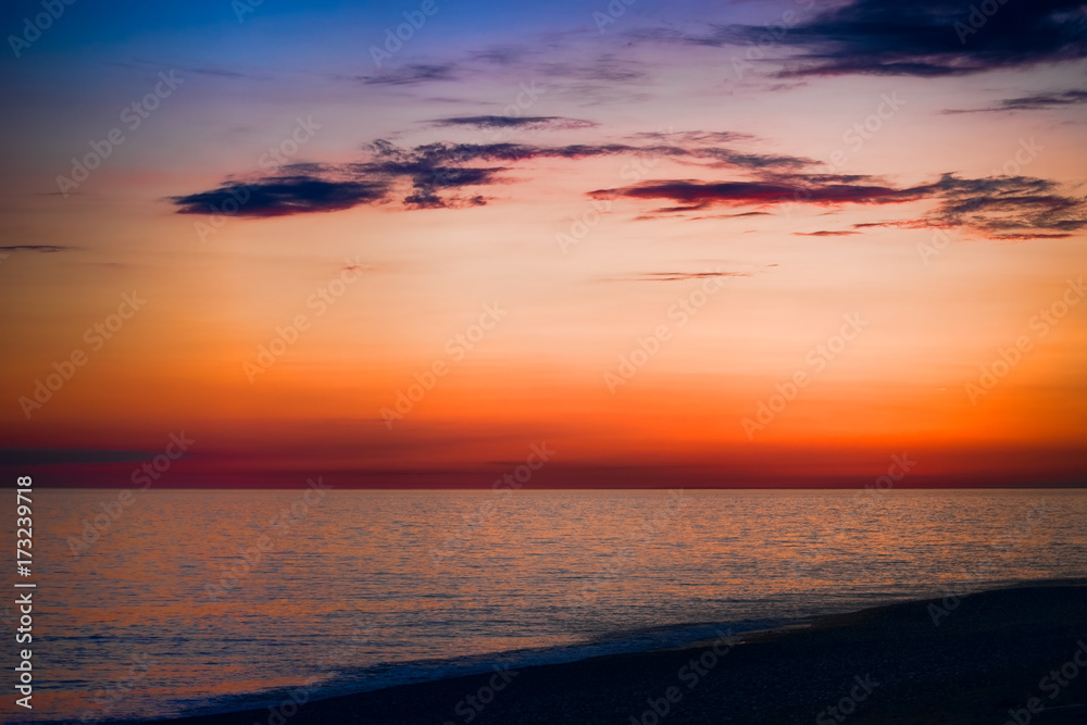 bright sunset over the blue sea with shimmering different colors in the clouds;