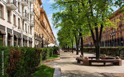 Beautiful landscape in residential area with trees, benches, alley, houses and blue sky in the background. Wonderful image. City infrastructure. Minsk, Belarus – May 16, 2016