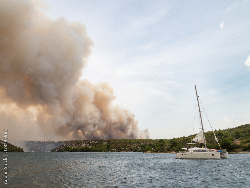 Forest fire in Croatia, summer natural disaster close to national park Krka, Sibenik region, boats and yachts escaping Skradin town from the smoke