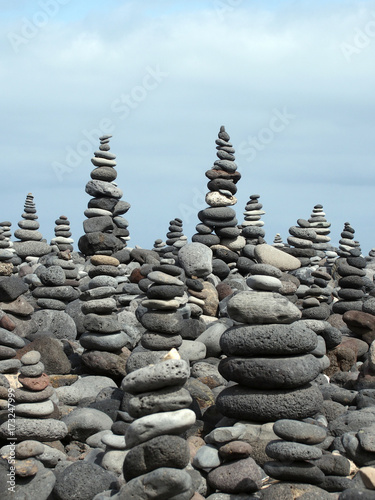 rock art piles and towers of grey stones and pebbles on a beach with blue sky