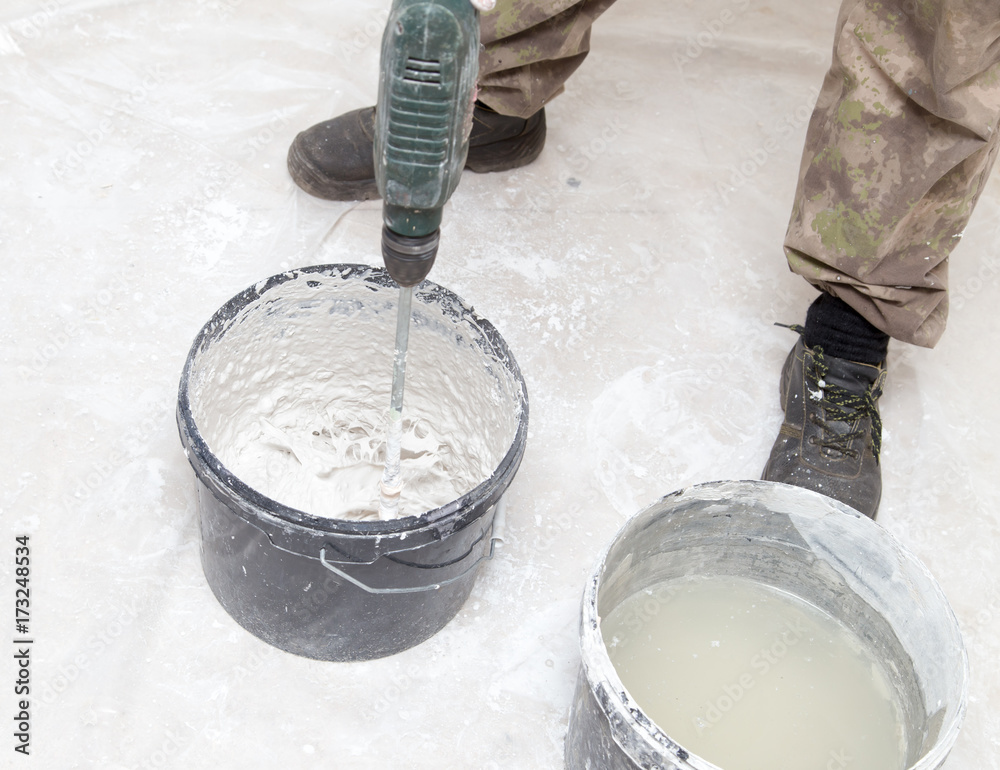 Fototapeta premium Worker mixes the solution with white plaster
