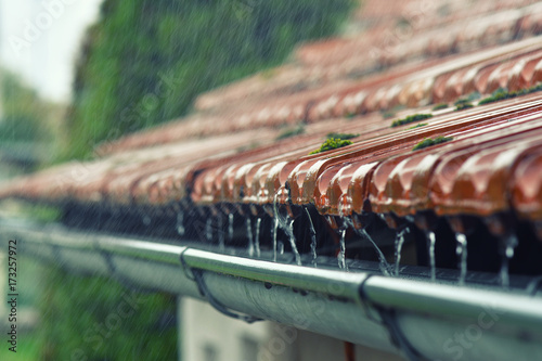 Drops of water flow into the eaves on the house in the rain. photo