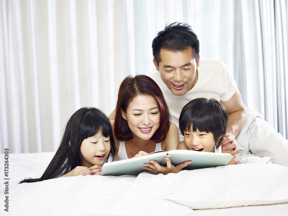 asian family with two children reading book in bed asian family with two children reading book in bed