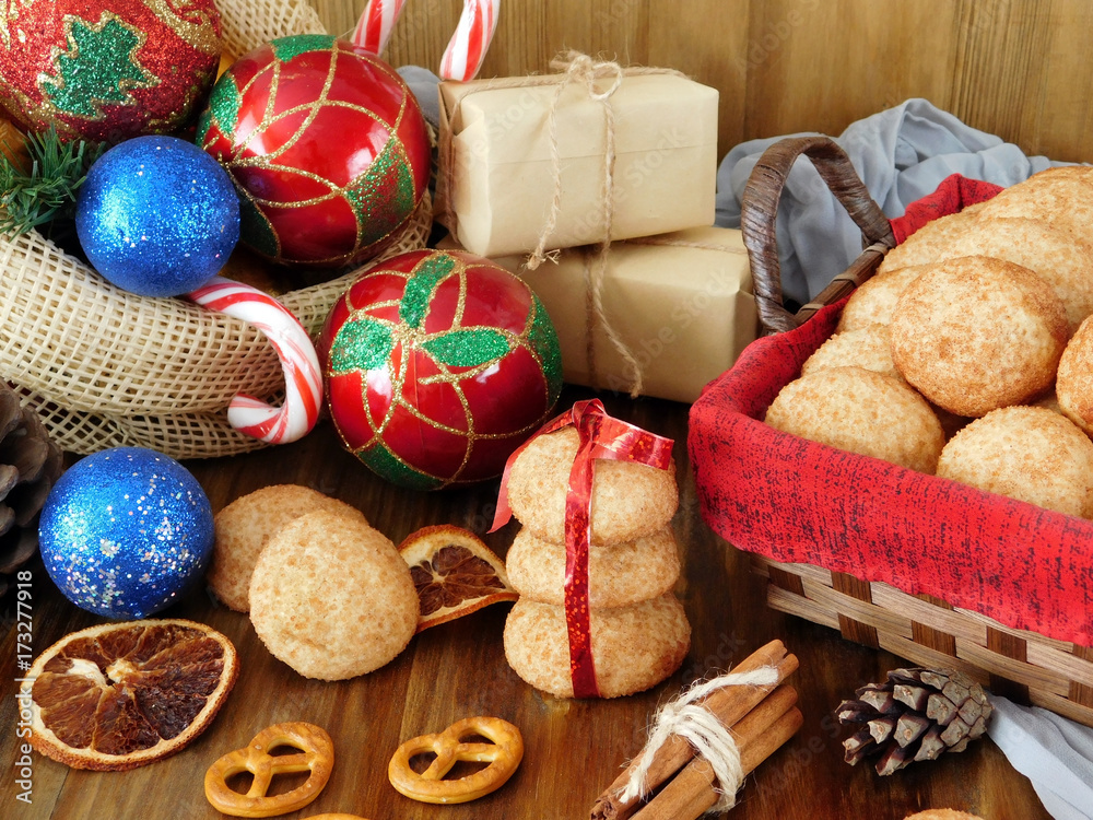 Biscuits with cinnamon in a wicker basket surrounded by present boxes and Christmas attributes on a wooden background Biscuits with cinnamon in a wicker basket surrounded by present boxes and Christmas attributes on a wooden background