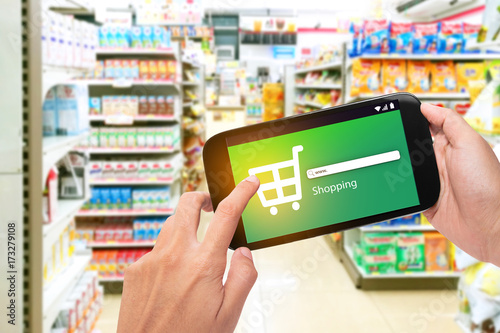 Hand holding mobile phone at supermarket checkout background, e coupon concept