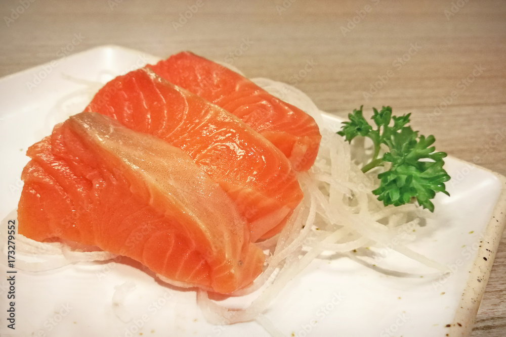 Salmon sashimi sliced on white julienned radish on white paper plate. Salmon sashimi sliced on white julienned radish on white paper plate.