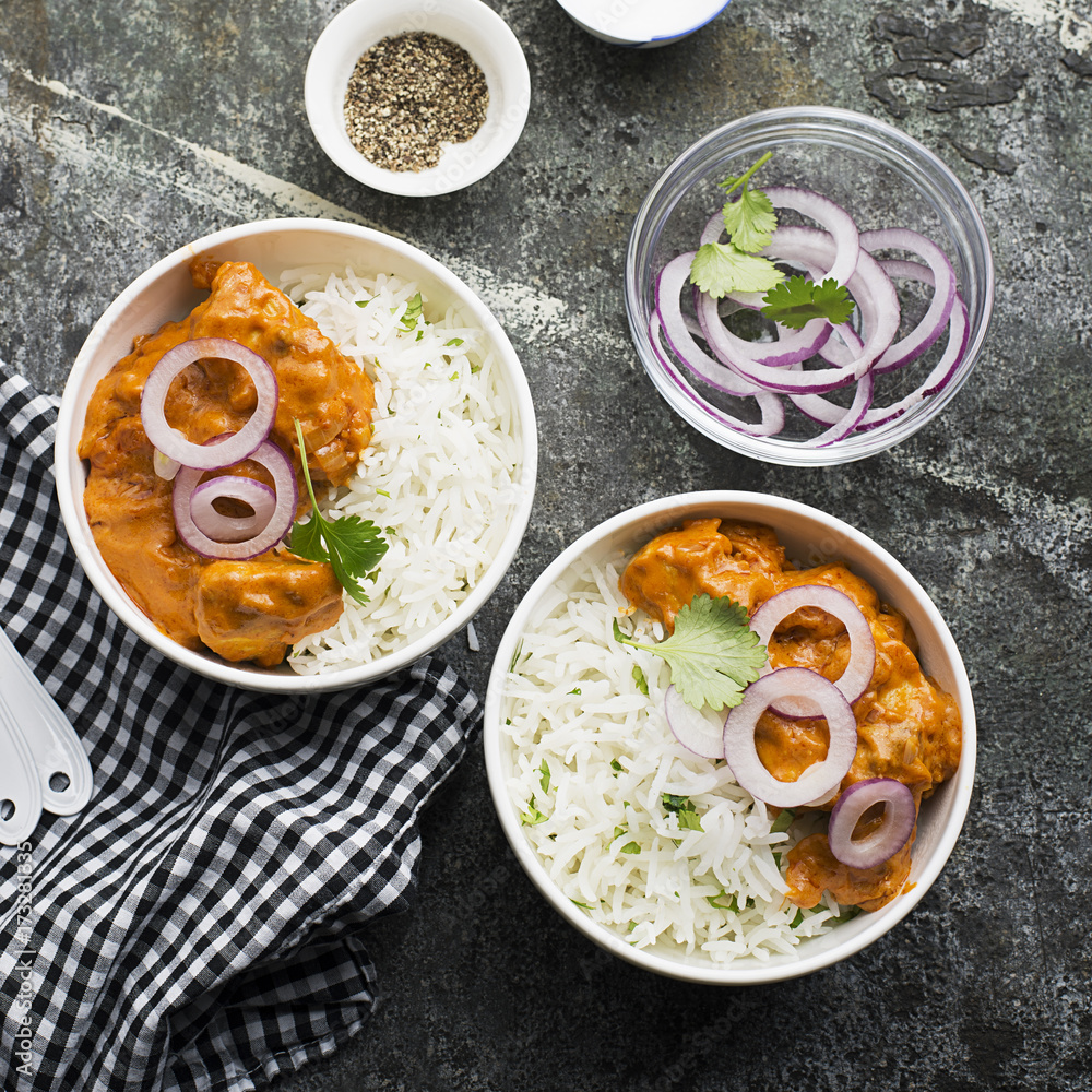Homemade dinner butter chicken on cream with spices, cream served with basmati rice in ceramic bowls with cilantro and sweet red onion. Top View.