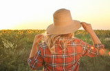 Young woman in wicker hat near sunflower field