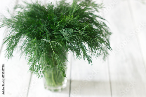 Fresh dill in a glass on a white wooden background. Rustic style, selective focus.