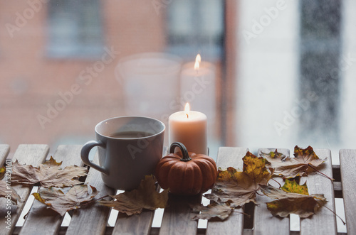 White cup of coffee or tea near a pumpkin and candle