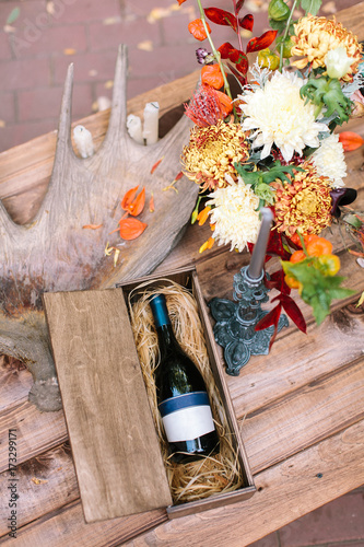 art, arranging, alcohol concept. on wooden table there is perfect still life with bottle of wine in special box, great horn of moose, candle in grey old holder and bunch of chrisantemums