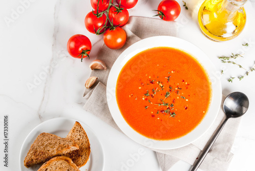 Tomato cream soup with olive oil and herbs, with toasted bread, on white marble background, copy space top view