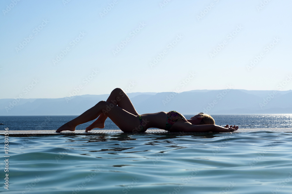 Girl lying on the edge of the pool merges with the sea.