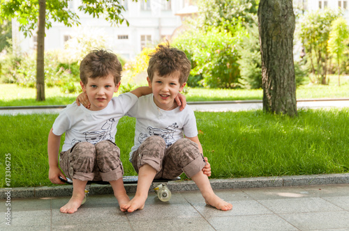 twin boys embraced sitting on skateboard outdoors in park