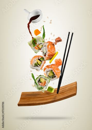 Flying sushi pieces served on wooden plate, separated on soft background