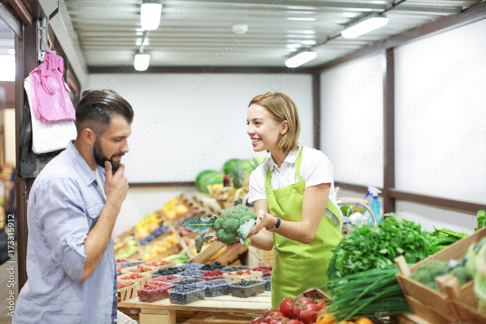 Naklejka premium Young shop assistant helping client at market