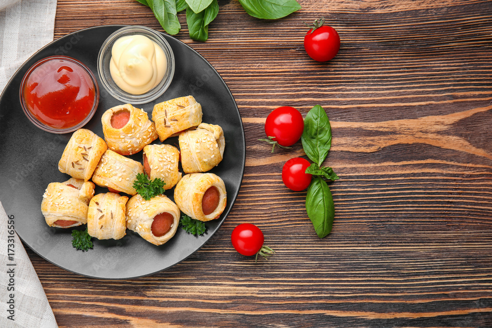 Plate with delicious sausage rolls on wooden background Plate with delicious sausage rolls on wooden background