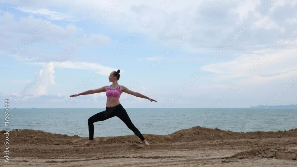 Girl practices yoga fitness exercise near the ocean beach in warrior pose 4k Girl practices yoga fitness exercise near the ocean beach in warrior pose 4k