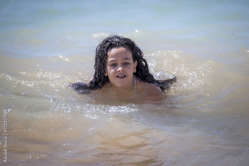 Obraz premium Niña morena bañándose en el mar y jugando con las olas.