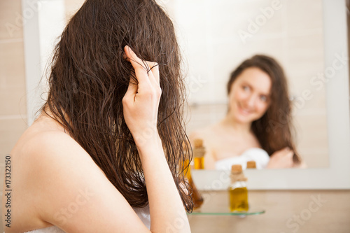 Smiling young woman applying oil mask to her hair