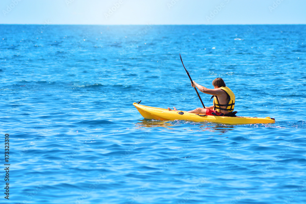 A man sails on a yellow canoe and rowing with an oar. Kayaking by the sea.