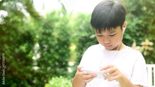 Young Asian Thai boy using a smartphone to play game and listen to music without care the surrounding.